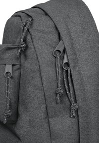 Šedý látkový batoh s nastavitelnými stahovacími šňůrkami, hladkou texturou a stylovým, minimalistickým designem. Doplněn odolnými kovovými prvky.