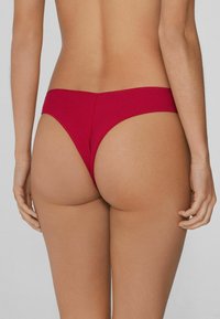 Red ribbed thong with a smooth finish, featuring a high-cut leg and minimal back coverage, designed to sit low on the hips.