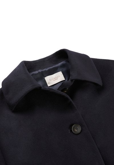 Granatowy wełniany płaszcz z wyłogowym kołnierzem, pojedynczym zapięciem na guzik i gładką podszewką. Posiada wewnętrzną metkę z logo oraz miękką teksturę.