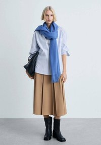 Blue scarf, striped button-up shirt, pleated brown skirt, and black ankle boots. Holding a black bag. Simple, balanced outfit with varying textures.