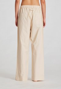 Pantaloni largi de culoare bej deschis, cu un tiv elastic strâns, o singură buzunar la spate, confecționați dintr-un material texturat.