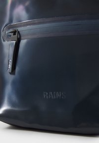 Navy waterproof bag with a smooth finish and a contrasting zipper. "RAINS" logo embossed on the front, emphasizing sleek design.