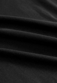 Sort stof med en glat, mat tekstur, der har bløde folder og subtile variationer i overfladens tone. Ingen mønstre eller udsmykninger synlige.