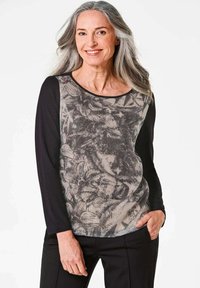 Langsleeve top met een zwart bloemenpatroon op een beige achtergrond, met effen zwarte mouwen. Zachte textuur en ronde halslijn.