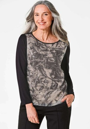 Langsleeve top met een zwart bloemenpatroon op een beige achtergrond, met effen zwarte mouwen. Zachte textuur en ronde halslijn.