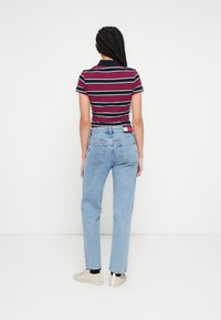 Burgundia ja mereväes triibuline polo särk, kombineeritud hele siniste sirgete teksadega. Tagumisel vööaugul on logomärk.