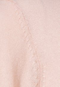 Tissu en tricot rose clair avec une finition texturée et des détails de coutures subtiles visibles le long de l'épaule et de la couture latérale.