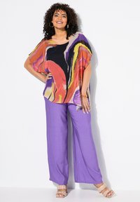 Multicolore, losse blouse met abstracte patronen; gecombineerd met lichtpaarse wijd-uitlopende broek; beige vetersandalen.
