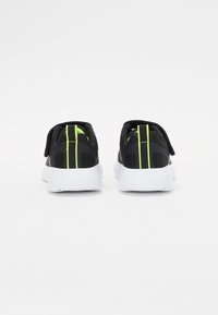 Zapatos deportivos negros con una parte superior de malla transpirable, con acentos en verde neón y una suela de goma blanca, mostrados desde atrás.