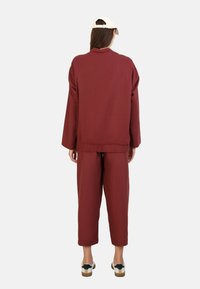 Ensemble bordeaux en deux pièces comprenant une veste ample avec un ourlet ajusté et un pantalon cropped assorti. Texture douce avec peu de détails de design.
