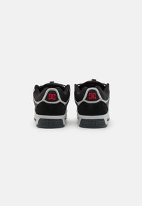 Adidași negri și gri, cu un superior din zamac și textil, guler căptușit și accente distincte de roșu pe călcâi. Tălpi din cauciuc plate.