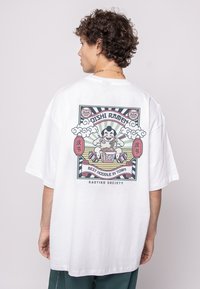 White oversized t-shirt featuring a colorful graphic on the back with a ramen theme, including lanterns and a character eating noodles.