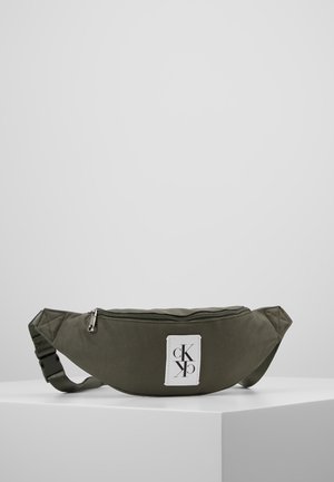 Olivgrüne Bauchtasche mit Reißverschluss oben und einem weißen rechteckigen Logo-Patch mit stilisierten schwarzen Buchstaben "cK" und "pK".