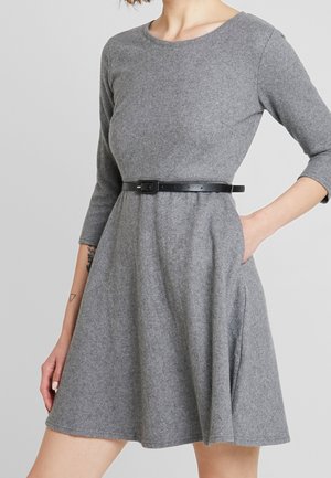 Grijze vilten jurk met lange mouwen, ronde halslijn, zwarte tailleceintuur en zijzakken. A-lijn model met een zachte textuur.