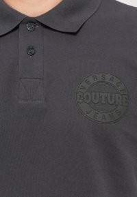 Svart polo skjorte med strukturert stoff, med en tre-knaps placket og en hevet, sirkulær logo preget på brystet.