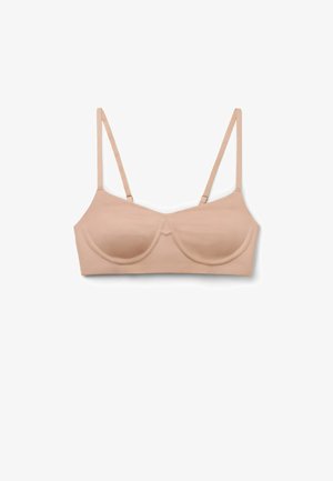 Soutien-gorge couleur nude, sans coutures, avec bonnets à armatures et fines bretelles réglables, posé à plat sur un fond blanc.