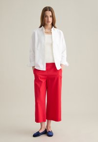 Witte blouse, crèmekleurige tanktop, rode cropped broek, blauwe flats en een gouden ketting. Eenvoudige, strakke lijnen en levendige kleuren.