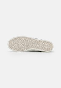 Rubber shoe sole in beige with a herringbone pattern, featuring a smooth edge and a reinforced heel for durability.