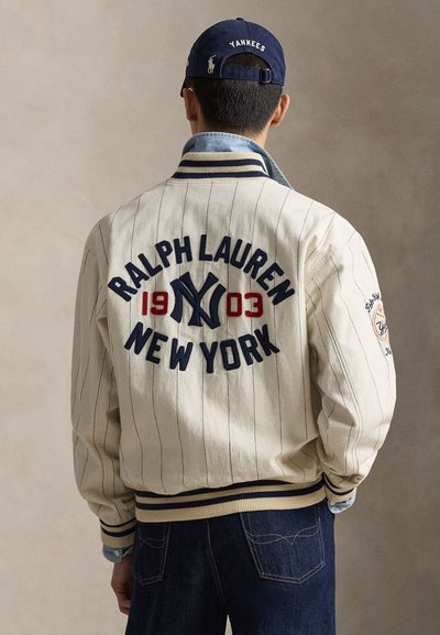 Kreemikas pesapalliriietus siniste triipudega, tikitud tekstidega "Ralph Lauren" ja "New York", soonikkoes varrukasuled ja krae.
