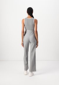 Graue maßgeschneiderte Hose mit hohem Bund und weitem Bein, kombiniert mit einem schwarz-weißen gestreiften Tanktop. Das Outfit wird mit weißen Sneakers abgerundet.