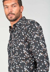 Camisa negra con patrón floral en blanco y naranja, de manga larga y cuello abotonado. Textura suave, diseño ajustado, botones visibles.