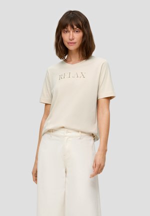 Light beige short-sleeve T-shirt with "RELAX" embroidered in a subtle font. Soft cotton material, paired with white wide-leg pants.