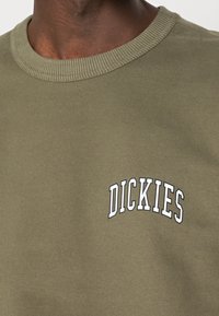 Felpa verde oliva scuro realizzata in morbido cotone, con collo a costine e il logo "DICKIES" ricamato in bianco sul petto.