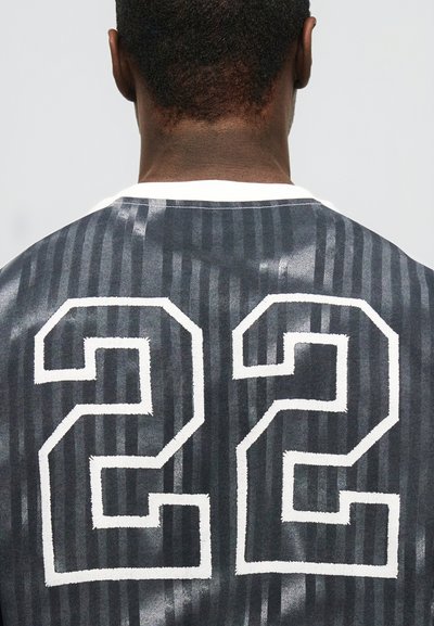 Πλάτη ενός ατόμου που φοράει αθλητική φανέλα με μαύρες και γκρι ρίγες και λευκό αριθμό 22 στην πλάτη.