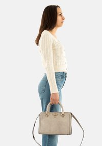 Borsa grigia textured con una forma strutturata, dotata di manico intrecciato e accessori metallici, tenuta in mano da una persona.