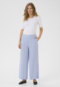Lichtblauwe, wijde broek met witte verticale strepen, gemaakt van een zachte stof. Heeft zijzakken en een platte tailleband.