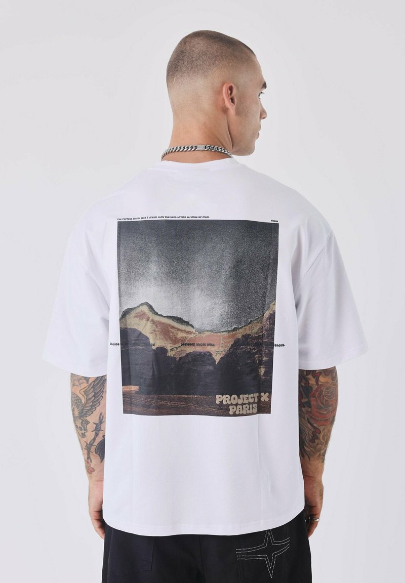T-shirt en coton blanc avec un grand imprimé graphique d'un paysage au dos, accompagné du texte "PROJECT X PARIS" en bas.