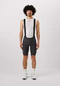 Shorts de cyclisme en gris foncé avec bretelles en maille noire, comportant un coussin de siège et des accents de logo. Design léger et ajusté.