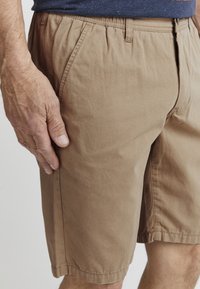 Korte tan bomullsshorts med elastisk midjebånd, sidelommer og en jevn tekstur. Har syddesømmer og minimalistiske designdetaljer.