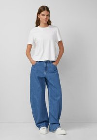 Baltās īsām piedurknēm T-krekls saskaņots ar gaiši zilām platām biksēm un baltām sporta apaviem, ar brīvu piegriezumu un minimālistisku dizainu.