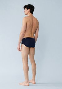 Marineblauwe herenslip met een contrasterende tailleband met tekst. De stof lijkt zacht, soepel en rekbaar, ontworpen voor comfort.
