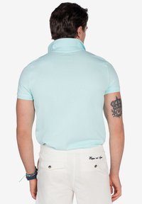 Polo de color azul claro con cuello elevado y mangas cortas, combinado con pantalones blancos que cuentan con dos bolsillos traseros y costuras decorativas.