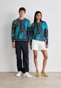Blue and multicolored patterned sweaters with long sleeves, paired with navy cargo pants and white shorts, complemented by yellow heeled sandals.