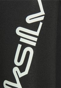 Leggings negros con un logotipo blanco en diagonal impreso a lo largo de un lado, hechos de una tela suave y elástica con una forma ajustada.