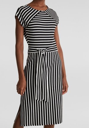 Black and white striped dress with a fitted top, wide shoulder design, a waist tie, and a knee-length skirt featuring side slits.