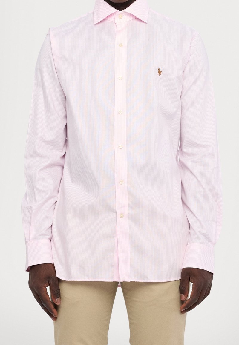 Světle růžová pruhovaná košile s knoflíkovým límcem a dlouhými rukávy. Obsahuje malé logo na hrudi a kulaté manžety.