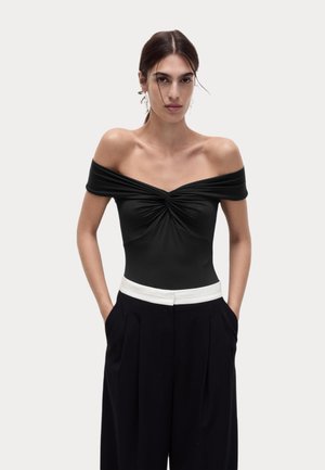 Černý body s odhalenými rameny a draped výstřihem, zkombinovaný s černými vysokými kalhotami s bílým pasem.