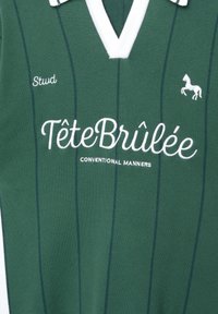 Grøn polo skjorte med hvide accenter og V-udskæring, med lodrette striber. Vist tekst omfatter "Stud," "TêteBrûlée," og "CONVENTIONAL MANNERS."