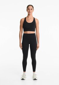 Svart sportbehå med breda axelband, hög midja svarta leggings. Slät tyg utan mönster, bärs med ljusa träningsskor.