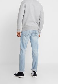 Světle modré džíny s rovný fit, s ohrnutými manžetami, nošené s šedým crewneck svetrem a černými vysokými teniskami.