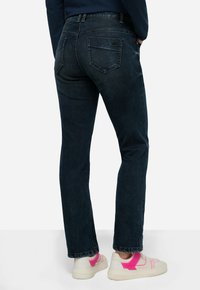 Jeans in denim blu scuro con taglio dritto, caratterizzati da tasche posteriori e leggeri sbiadimenti, abbinati a sneakers bianche con dettagli rosa.