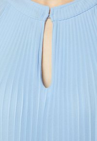 Himmelblaues, plissiertes Gewebe mit einem Schlüssel-ausschnitt und einer kleinen Schlaufe zum Schließen. Glatte Textur und gleichmäßige Nähdetails.