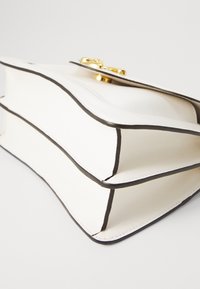 Witte leren handtas met zwarte accenten, rechthoekige vorm en een gouden sluiting. Bevat twee compartimenten met zichtbare stiksels.