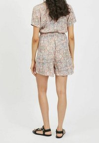 Kortärmad, rosa mönstrad jumpsuit med cinch i midjan och lösa shorts. Materialet har en slät yta med dekorativa blommönster.