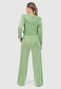 Ensemble de loungewear en velours vert clair comprenant une veste à capuche et un pantalon large, mettant en avant une texture douce et une coupe décontractée.