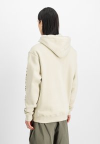 Ljusbeige hoodie med en stor huva, långa ärmar och ribbade muddarna. Slät textur med minimala sömmar och en enkel design.